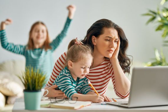 Une femme en télétravail semble stressée, ses enfants jouent près d'elle.