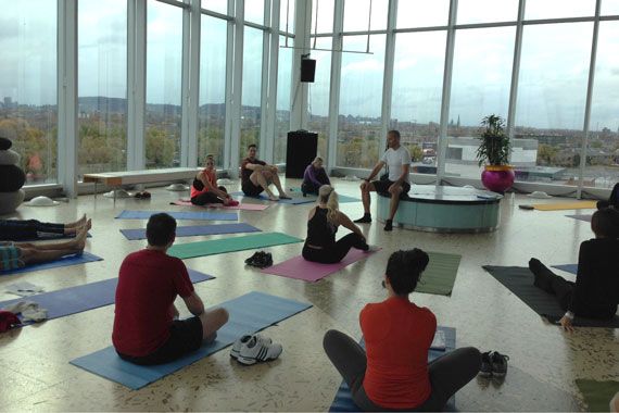 Des gens sont assis sur des tapis de yoga dans une grande salle vitrée.